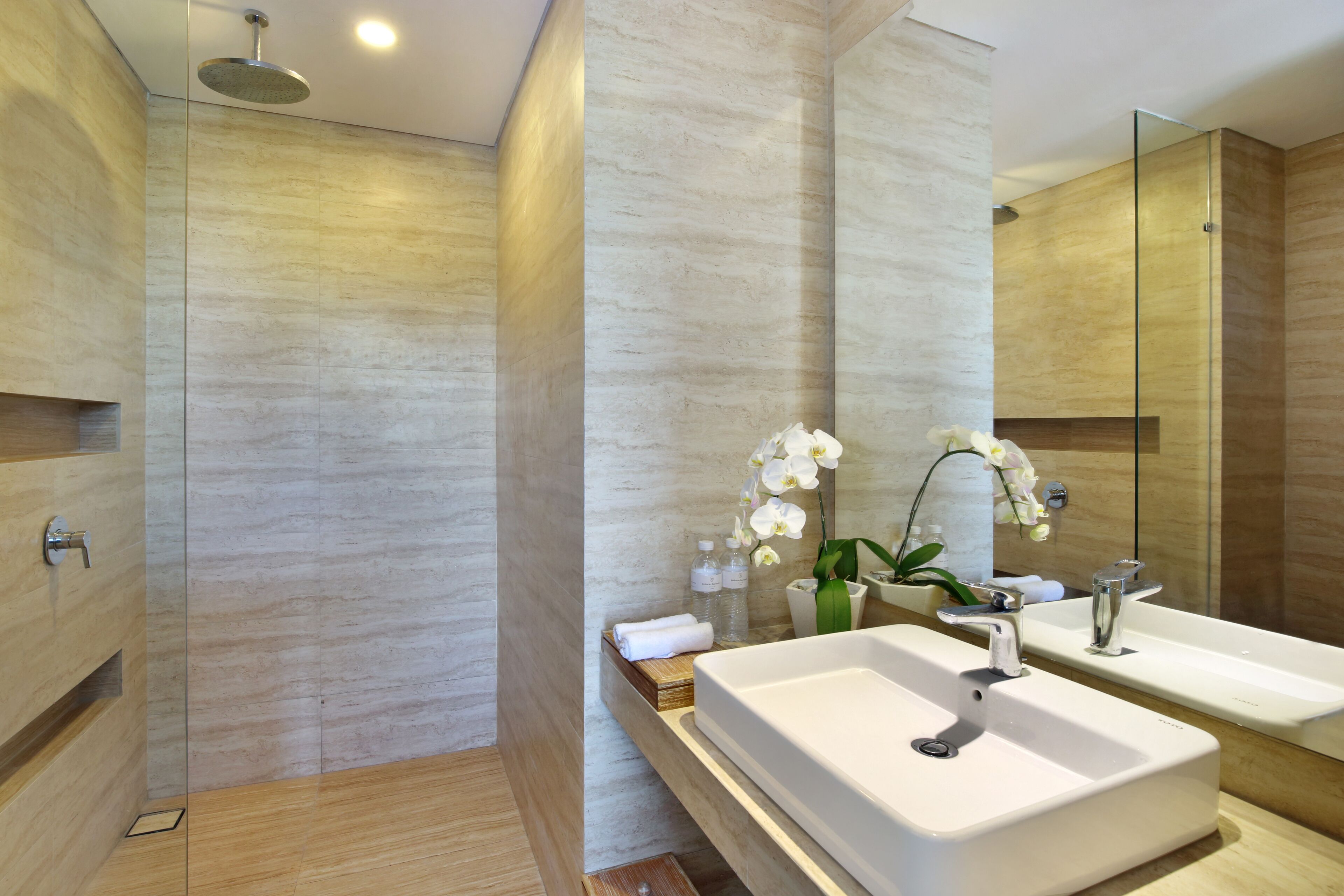 Un baño moderno con ducha de vidrio, un espejo grande y un lavabo blanco.