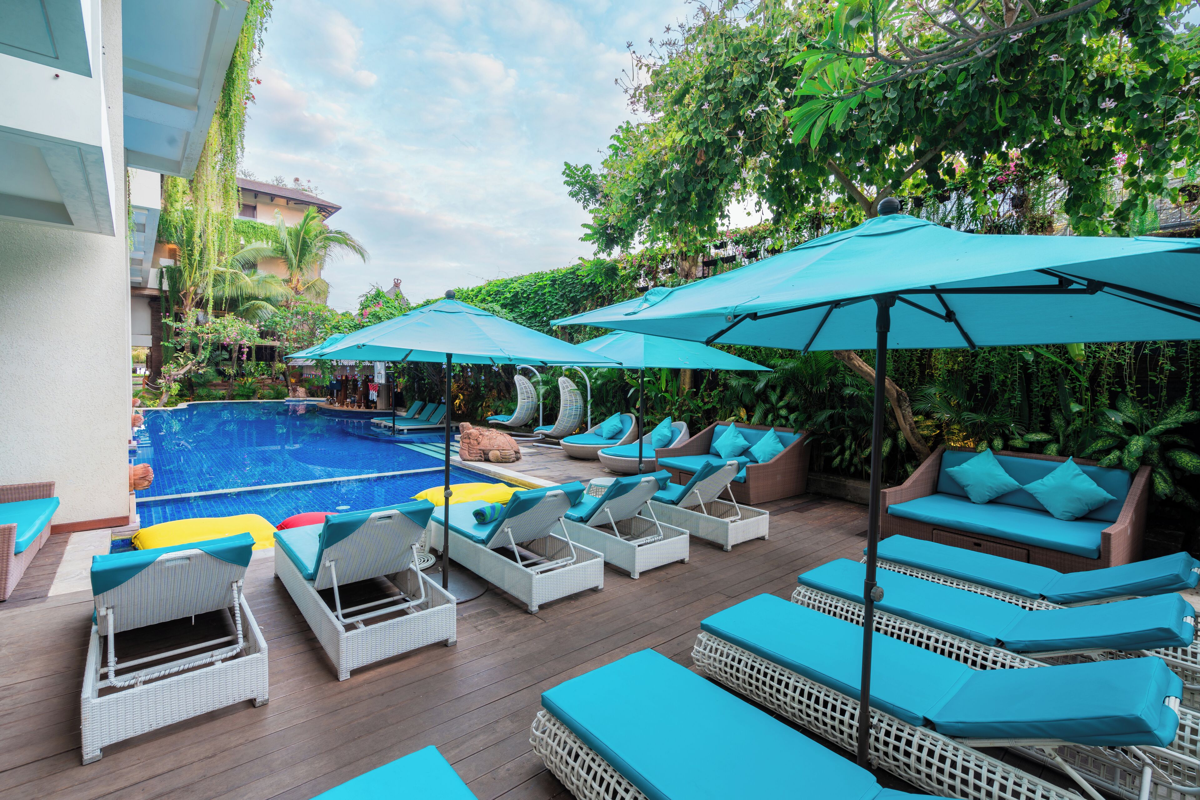 Zona junto a la piscina con sillones de descanso y sombrillas, piscina y abundante vegetación.