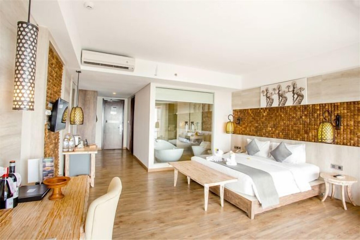 A modern hotel room with a wooden floor, a bed with white bedding, a desk, and a seating area.