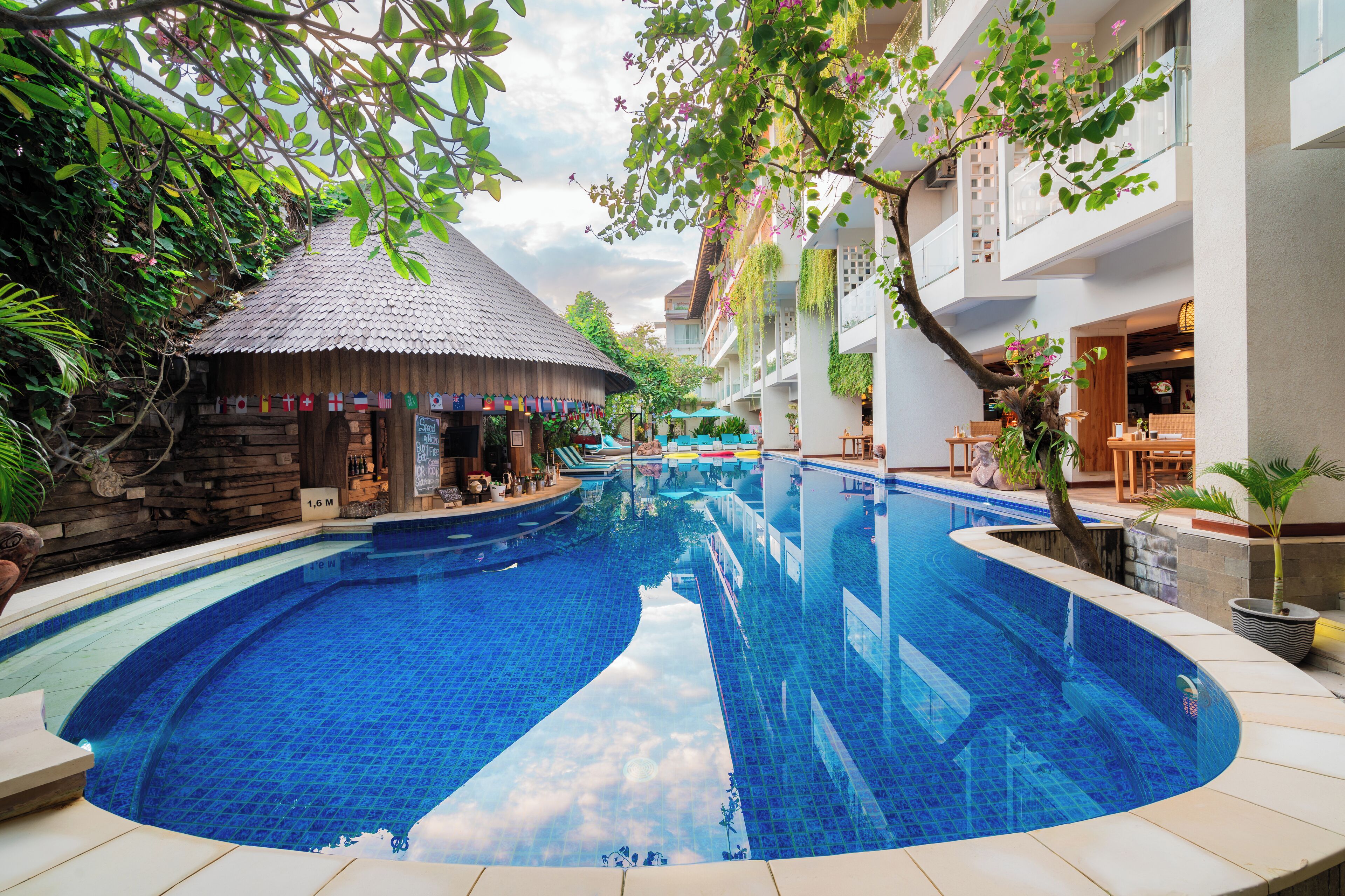 A large indoor swimming pool with a tropical setting, including a thatched-roof hut and lush greenery.