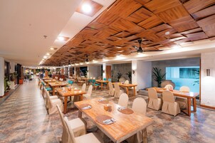 Un restaurante espacioso con varias mesas y sillas, techo de madera y plantas en macetas.