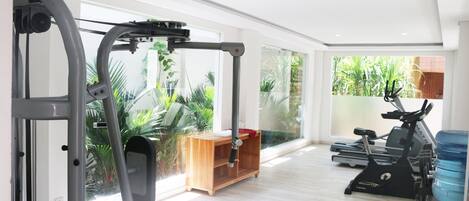 A spacious gym with a variety of exercise equipment, large windows offering views of greenery, and a modern interior design.
