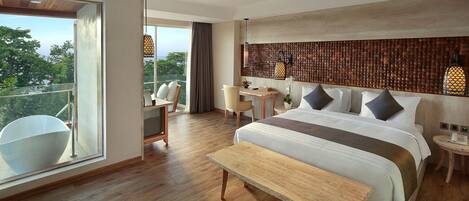 A modern hotel room with a large bed, a wooden bench, a desk, and a balcony with a view of the trees.