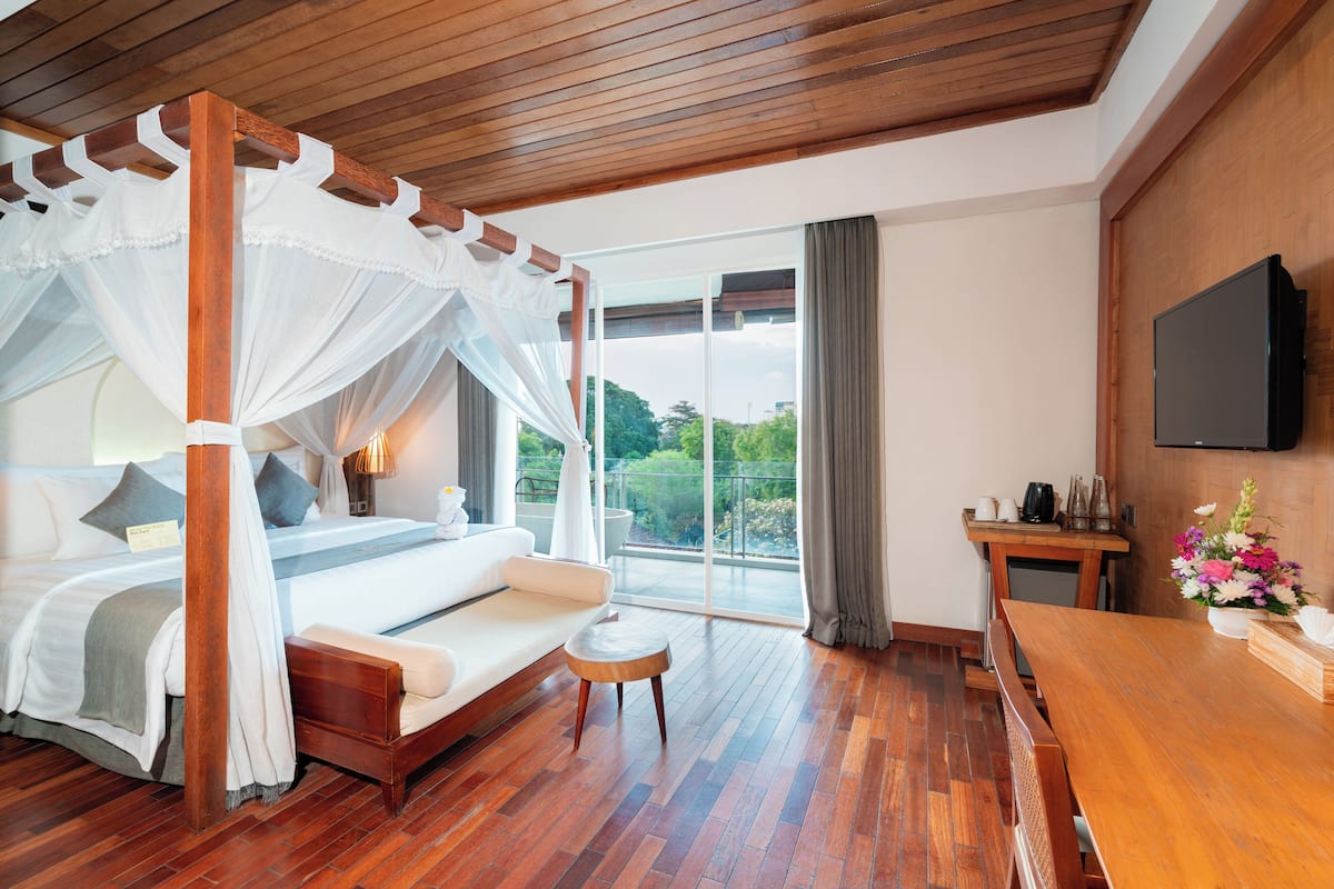 A bedroom with a four-poster bed, a sofa, a wooden table, and a TV on the wall.