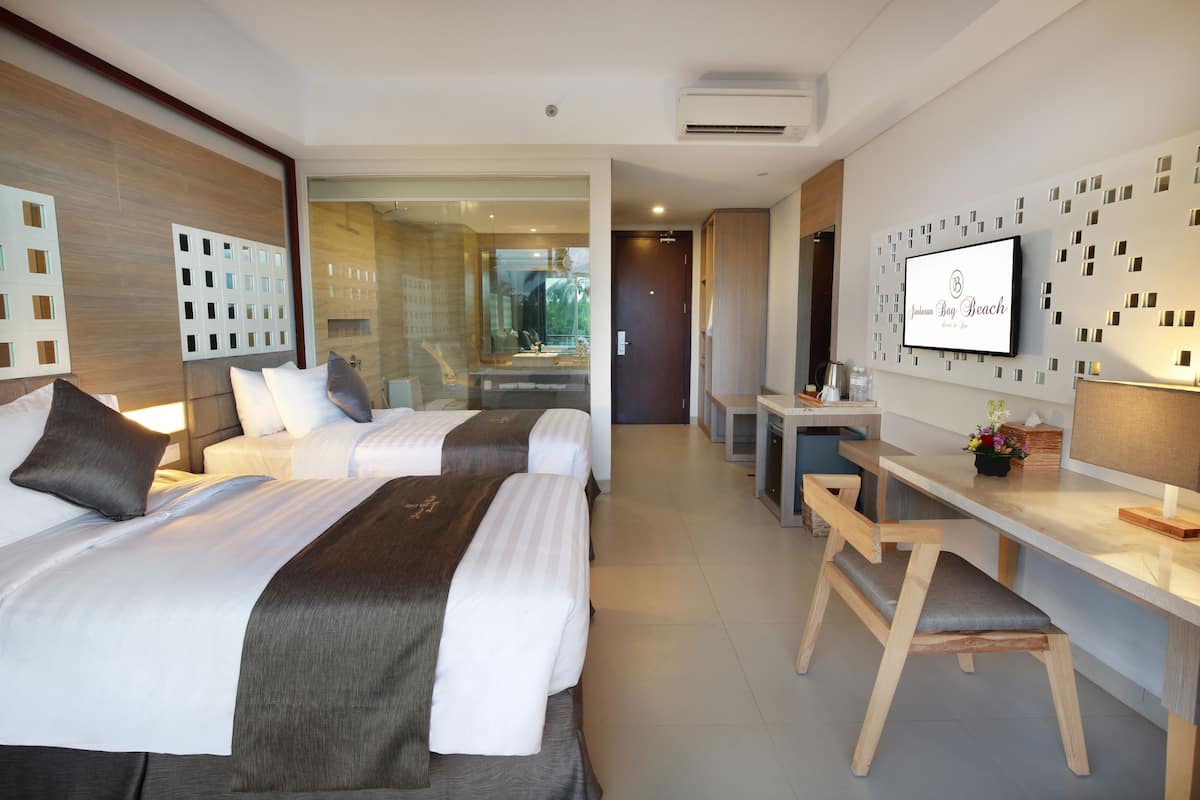 A modern hotel room with two beds, a desk, and a TV.