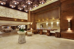 Um lobby espaçoso com área de estar central, balcão de recepção e parede decorativa com motivos florais.