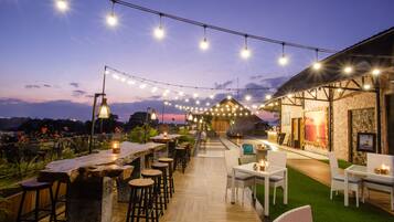 Un área de bar al aire libre con luces colgantes, taburetes de madera y una pared de piedra.