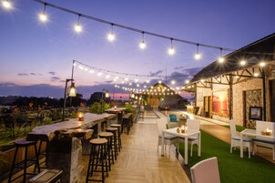 Un área de bar al aire libre con luces colgantes, taburetes de madera y una pared de piedra.