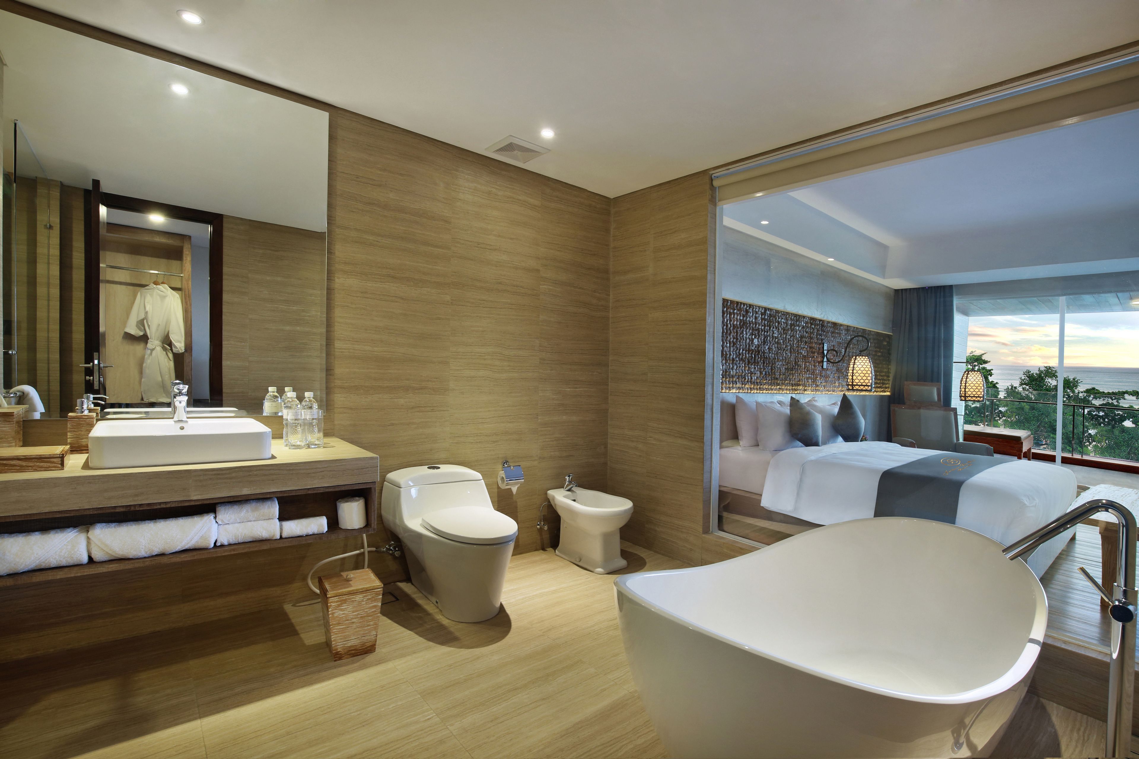 Un baño moderno con una bañera grande, un inodoro y un lavabo. Hay un espejo grande sobre el lavabo y una ventana con vistas a la ciudad.