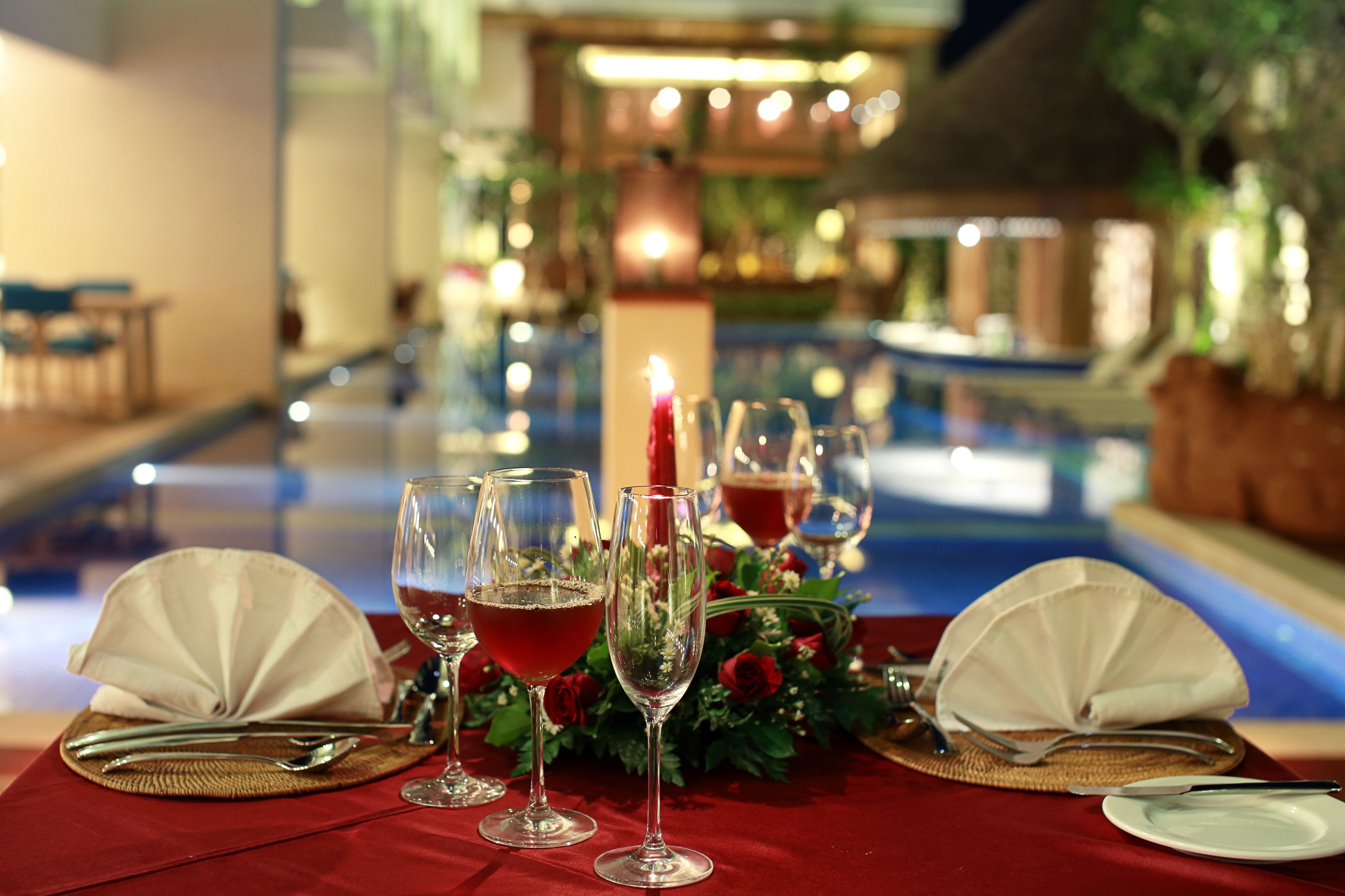 A table set for a meal with a pool view, including a candle and floral decorations.