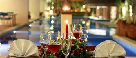 A table set for a meal with a pool view, including a candle and floral decorations.