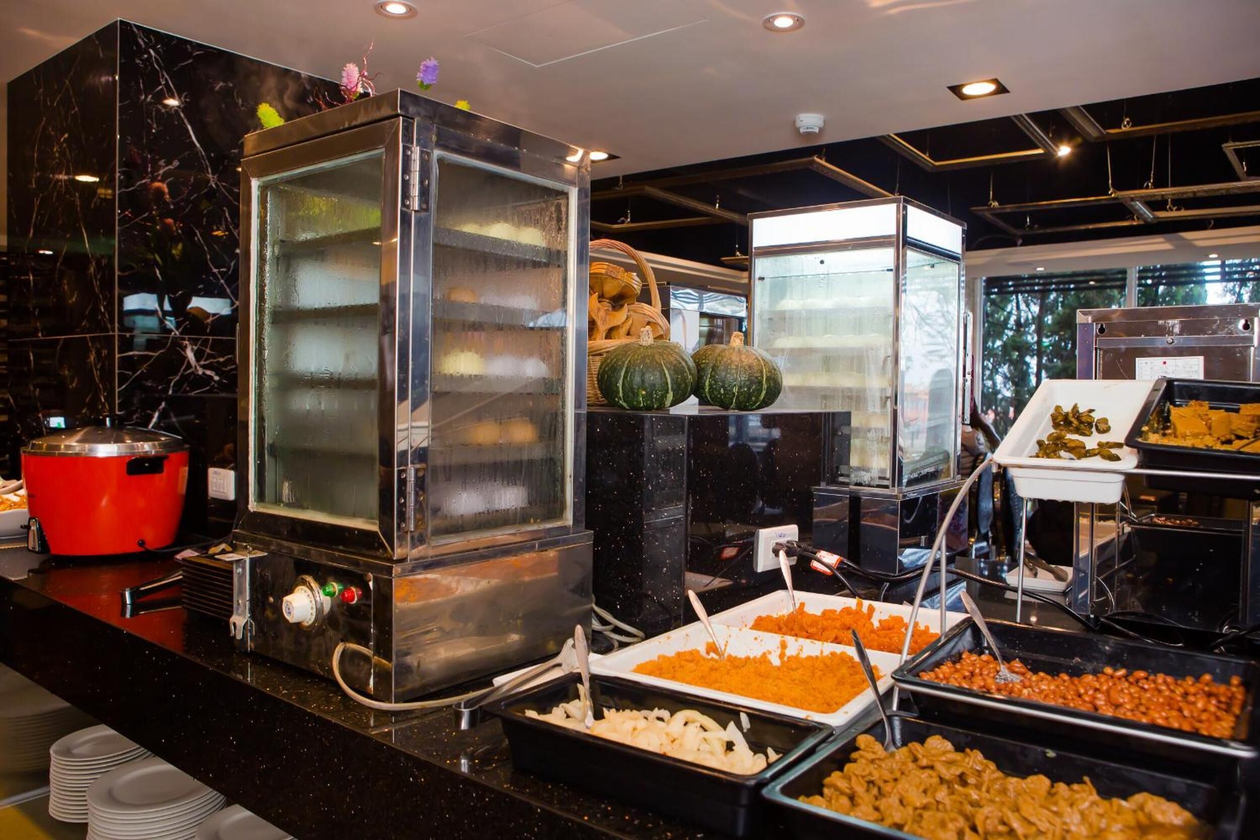 A buffet area with various food stations, including a glass display case and a red pot.
