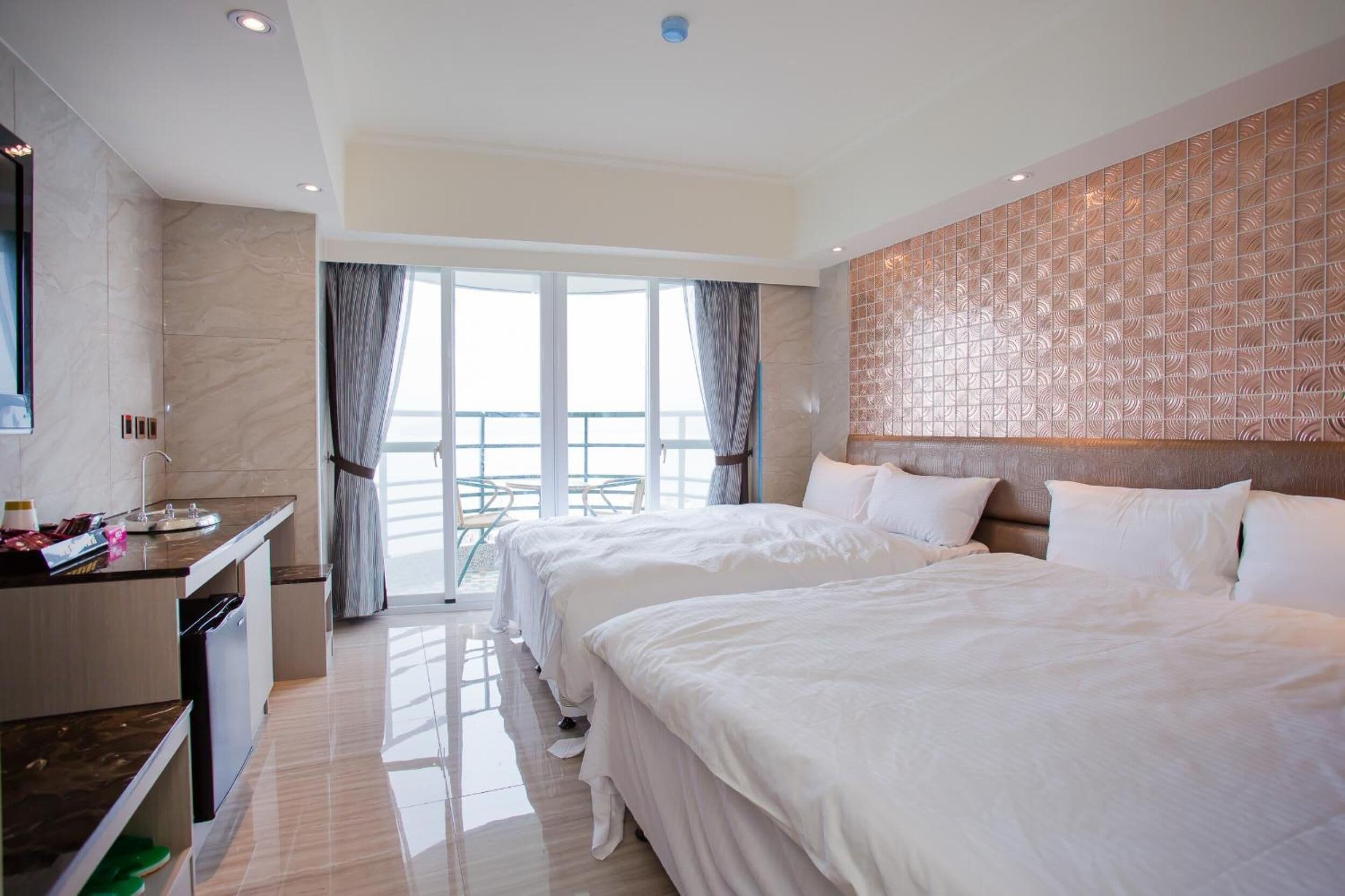A hotel room with two beds, a kitchenette, and a balcony with a view.