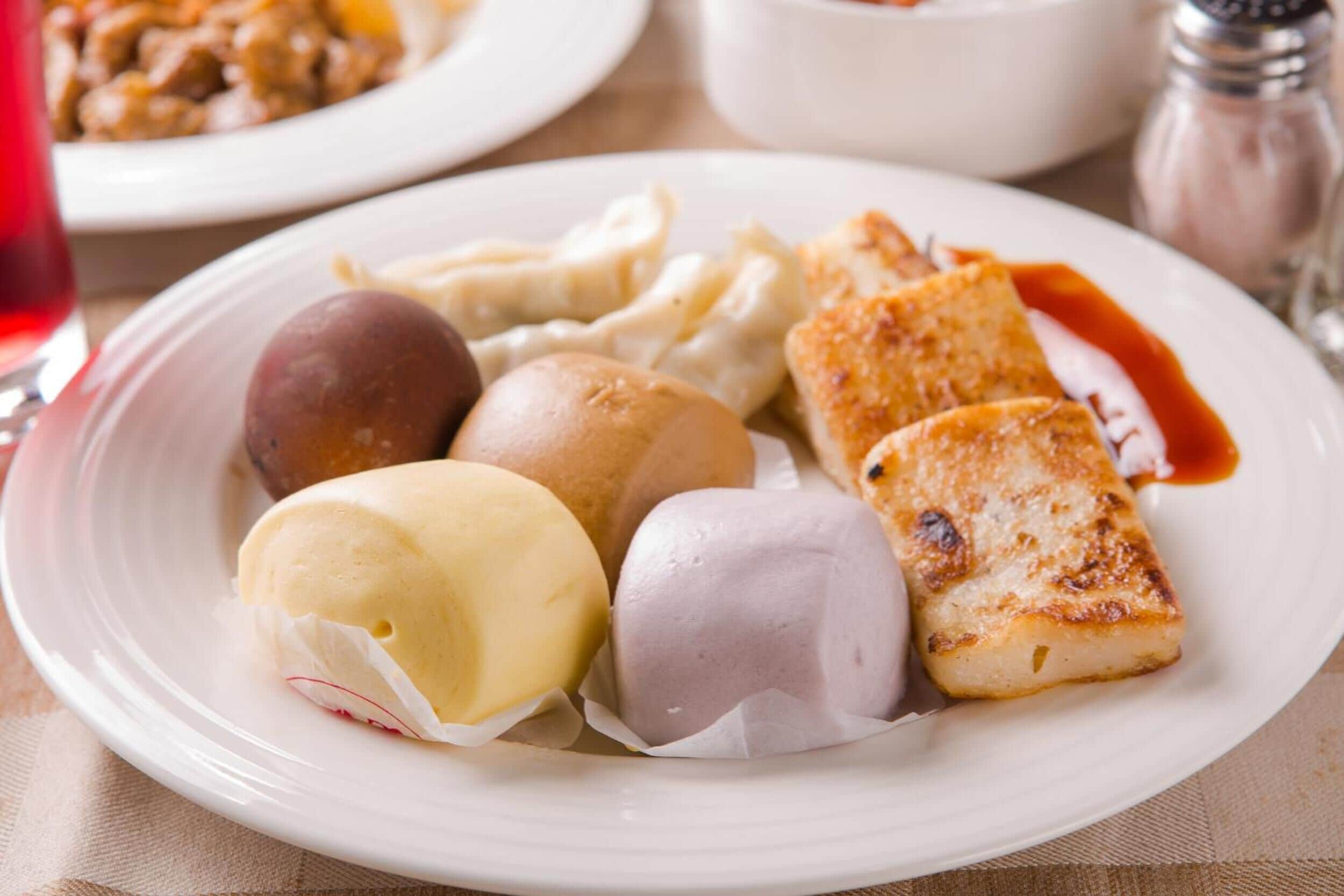 Een bord met diverse etenswaren, waaronder dumplings, een stuk brood en een dessert.