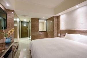 Habitación de hotel con una cama grande, pared de mármol, televisor de pantalla plana y baño con ducha e inodoro.