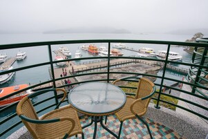 Un balcón con sillas de mimbre y una mesa de vidrio con vistas a un puerto deportivo lleno de barcos.