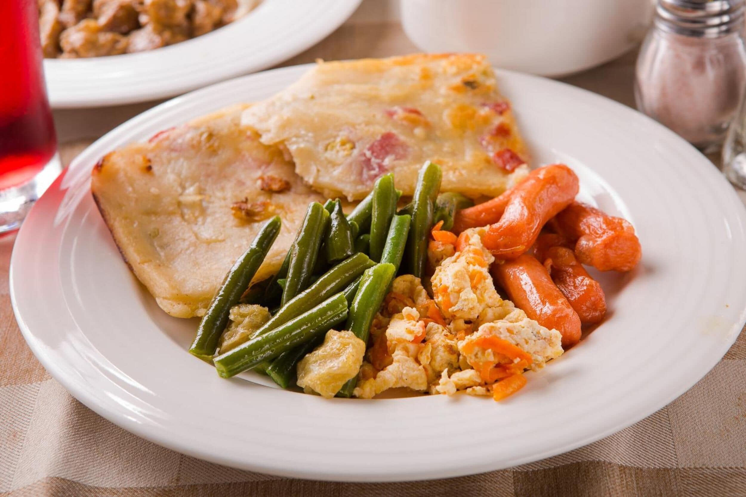 Un plato de comida con un trozo de pollo, judías verdes, zanahorias y huevos revueltos.