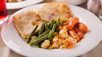 A plate of food with a piece of chicken, green beans, carrots, and scrambled eggs.