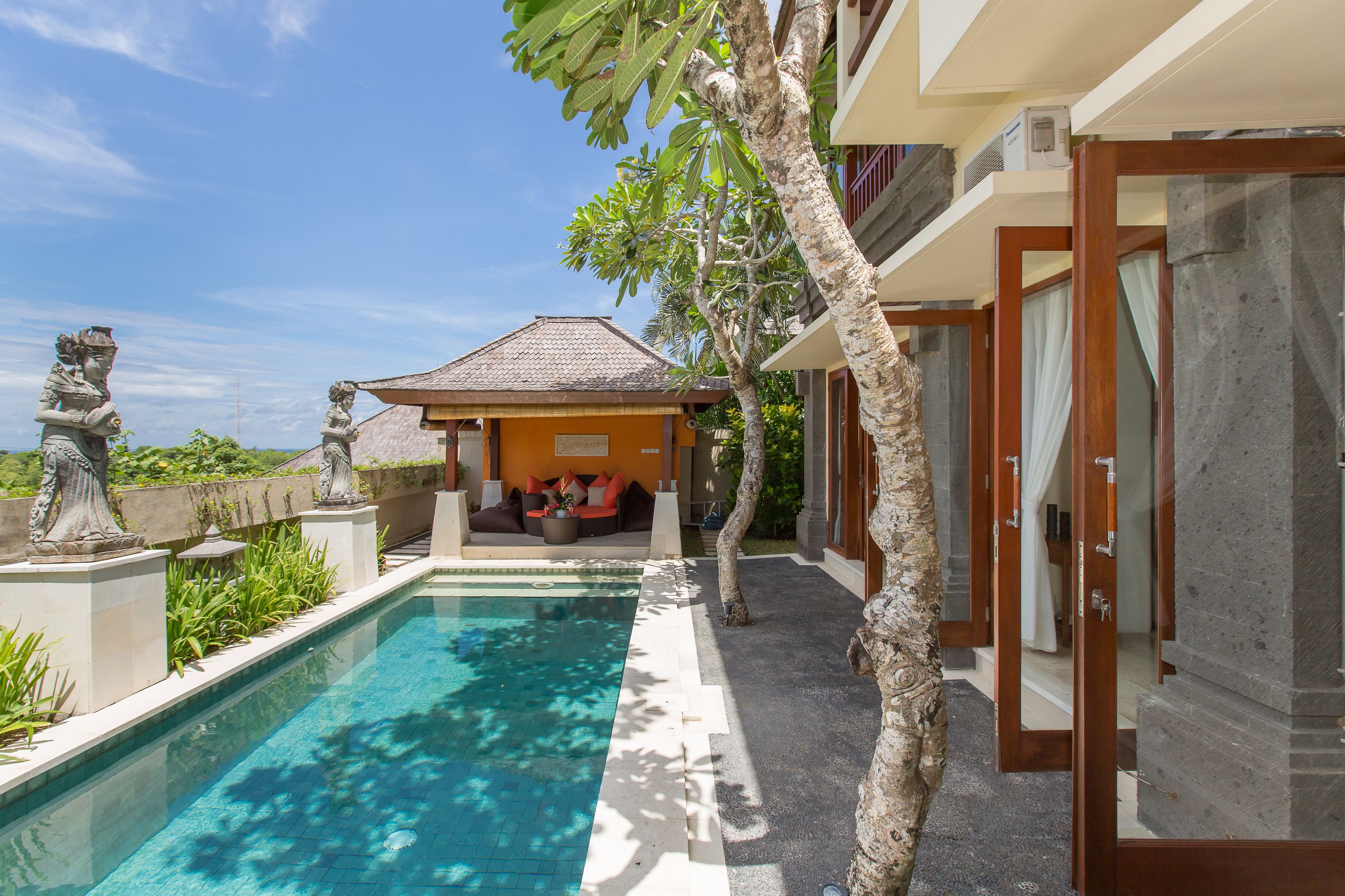 A swimming pool with a clear blue water, a wooden deck, and a building with a tiled roof in the background.