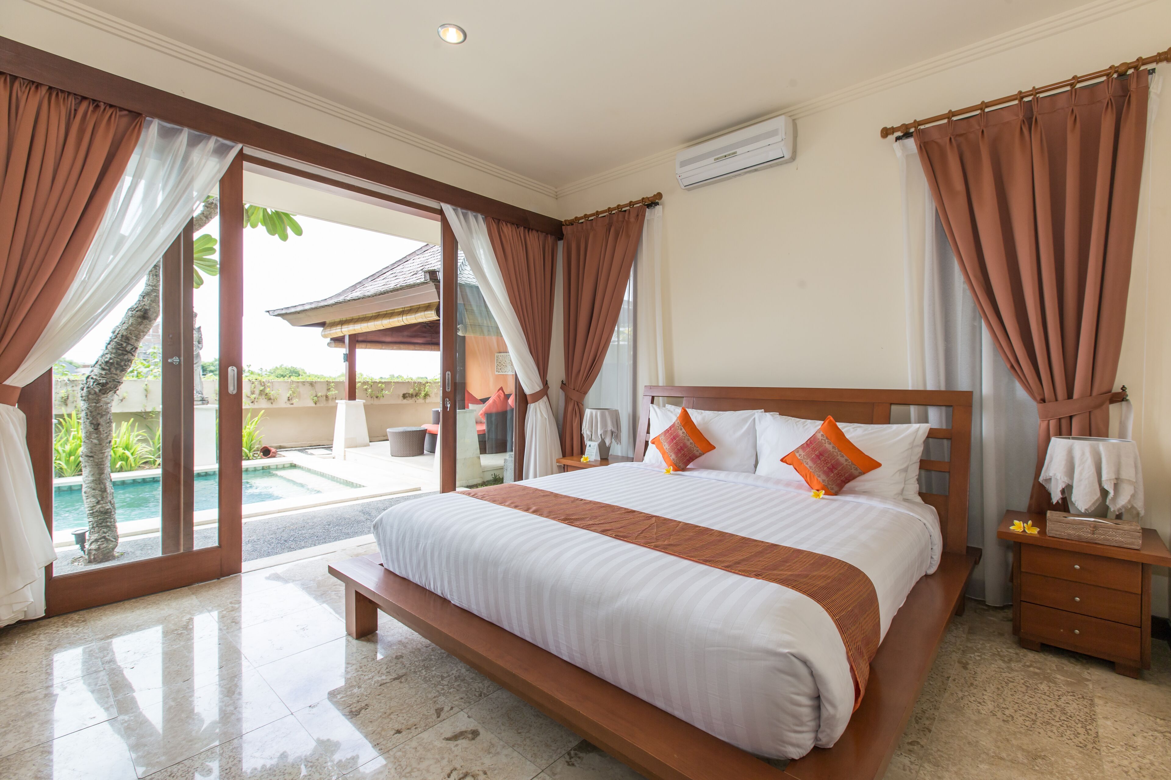 A spacious bedroom with a large bed, a wooden nightstand, and a view of a swimming pool.