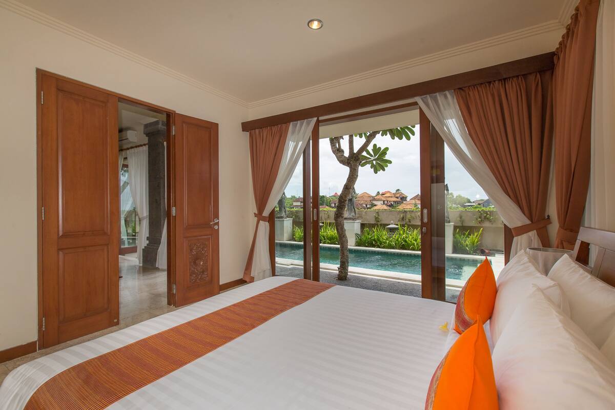 A hotel room with a large bed, a view of a swimming pool, and a wooden door.