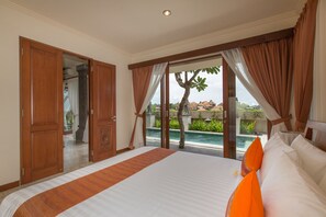 A hotel room with a large bed, a view of a swimming pool, and a wooden door. - Villa Lidwina by Nagisa Bali (Ungasan)