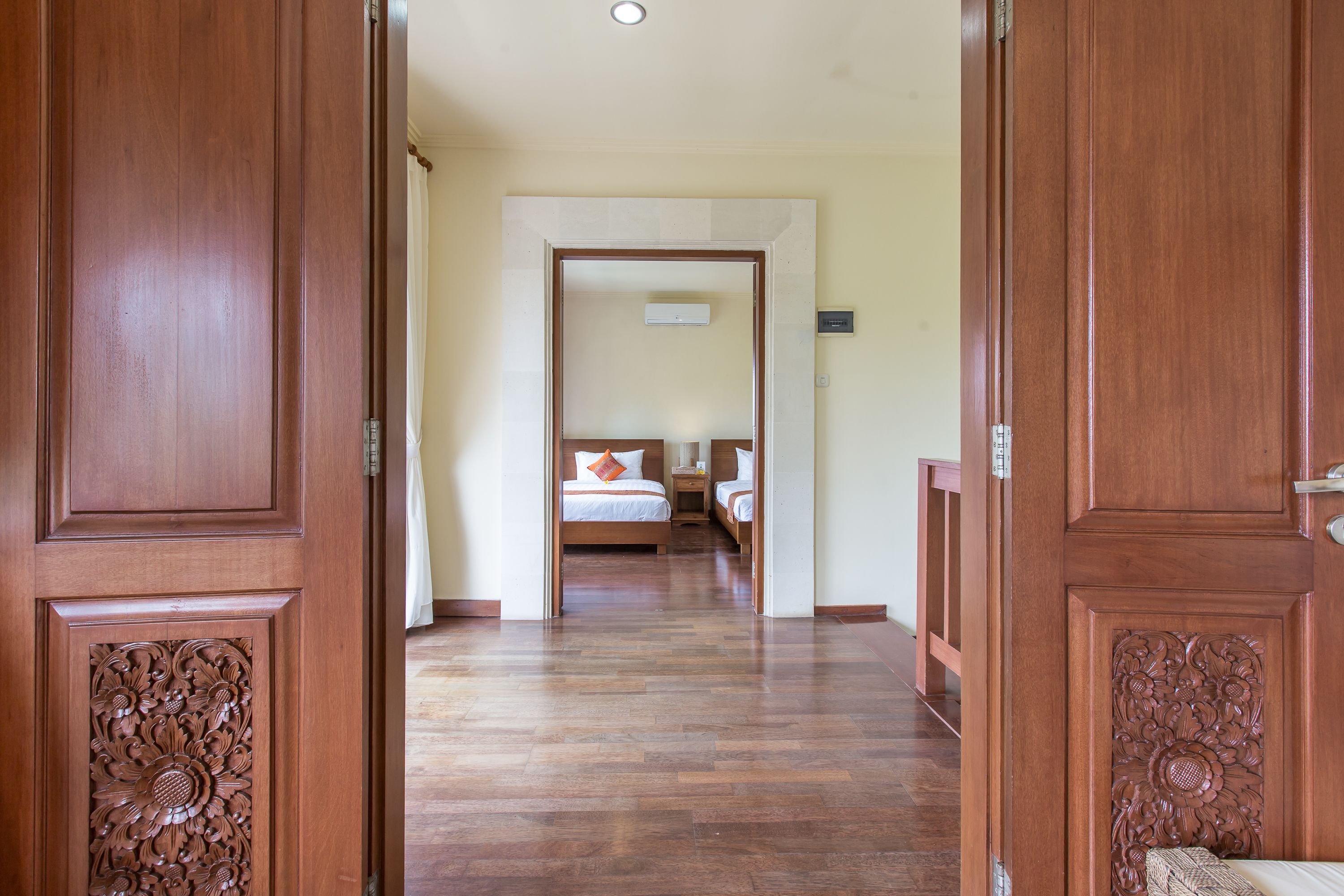 Un pasillo de madera que conduce a un dormitorio con cama, mesita de noche y un interruptor de luz en la pared.