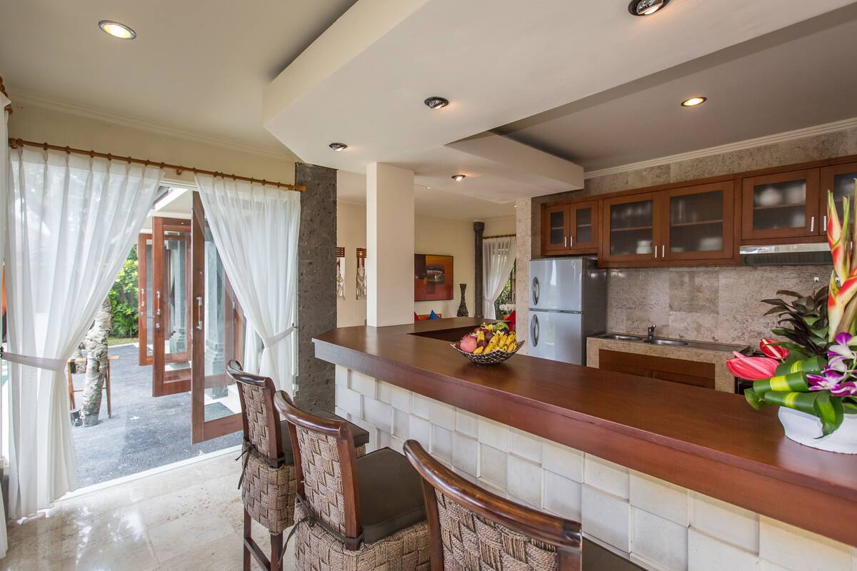 A modern kitchen with a marble countertop, wooden cabinets, and a dining area with wicker chairs.