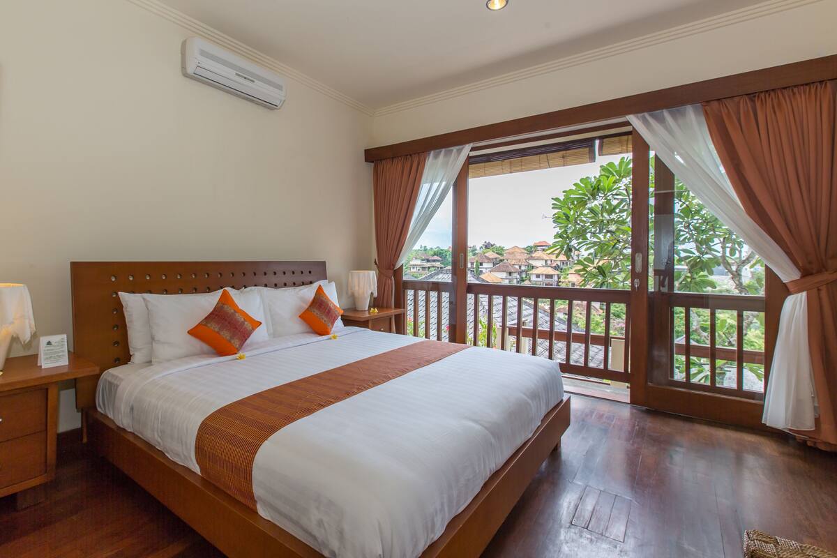 A spacious bedroom with a large bed, wooden headboard, and a balcony with curtains.
