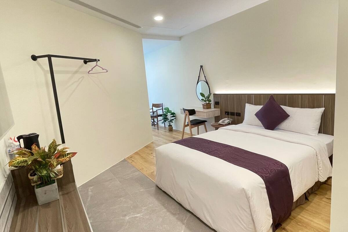 Une chambre d’hôtel moderne, dotée d’un grand lit, d’un bureau, d’une chaise, d’un porte-vêtements et d’une plante en pot.