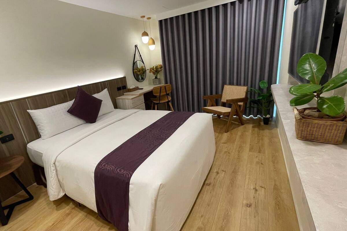 Une chambre d’hôtel comprenant un lit, une table de chevet, une chaise, une plante en pot et un bureau avec une chaise.