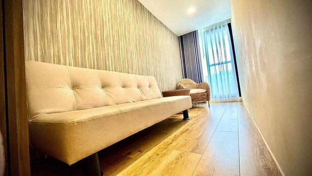 Una sala de estar moderna con un sofá beige, un sillón de mimbre, piso de madera y un ventanal con cortinas.