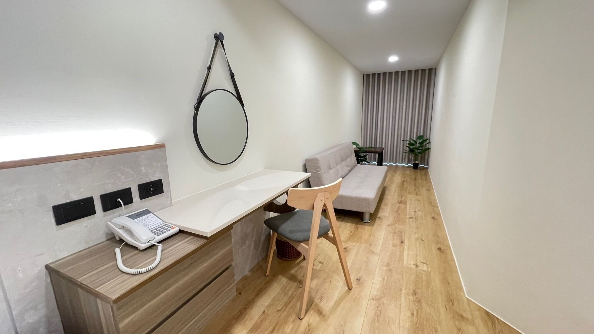 A modern, minimalist room with a wooden desk, a grey sofa, and a small table with a plant.