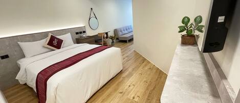A modern hotel room with a large bed, a bedside table, a nightstand, a chair, a small table with a plant, and a wall-mounted TV.