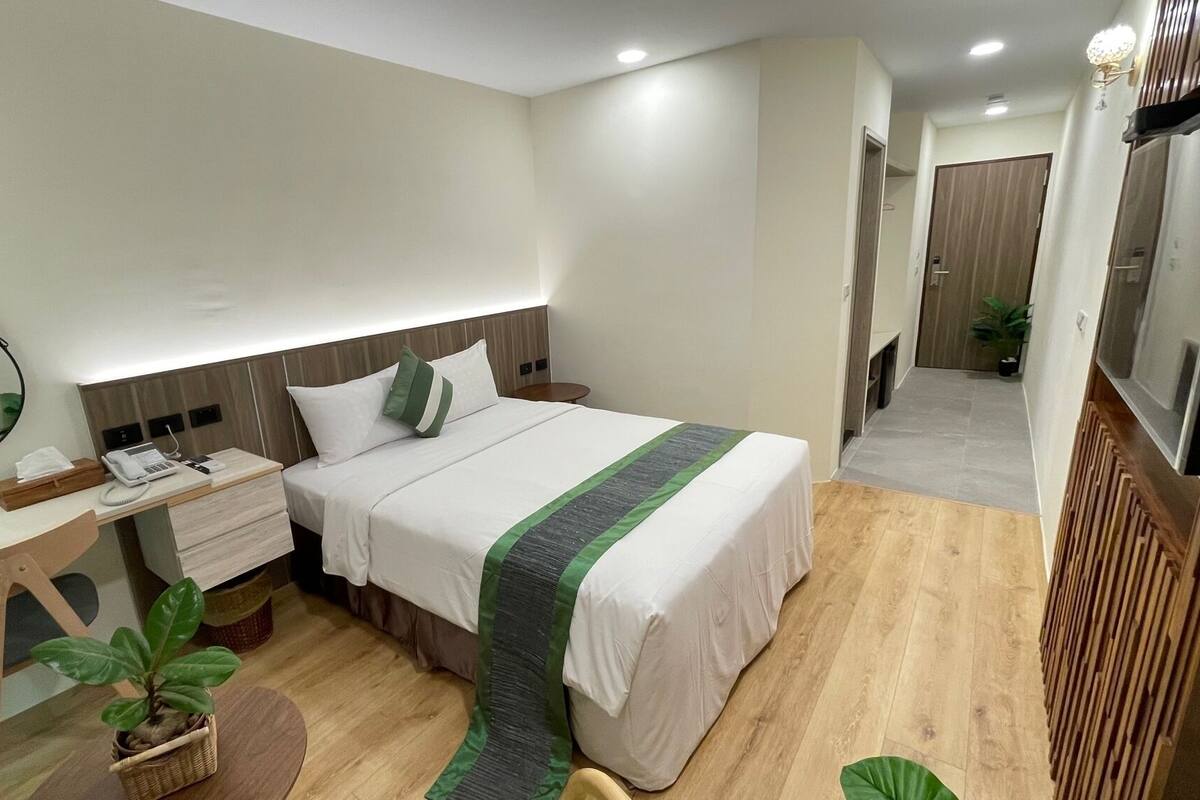 Une chambre d’hôtel avec un lit, une table de chevet, une lampe, un miroir et une petite plante.