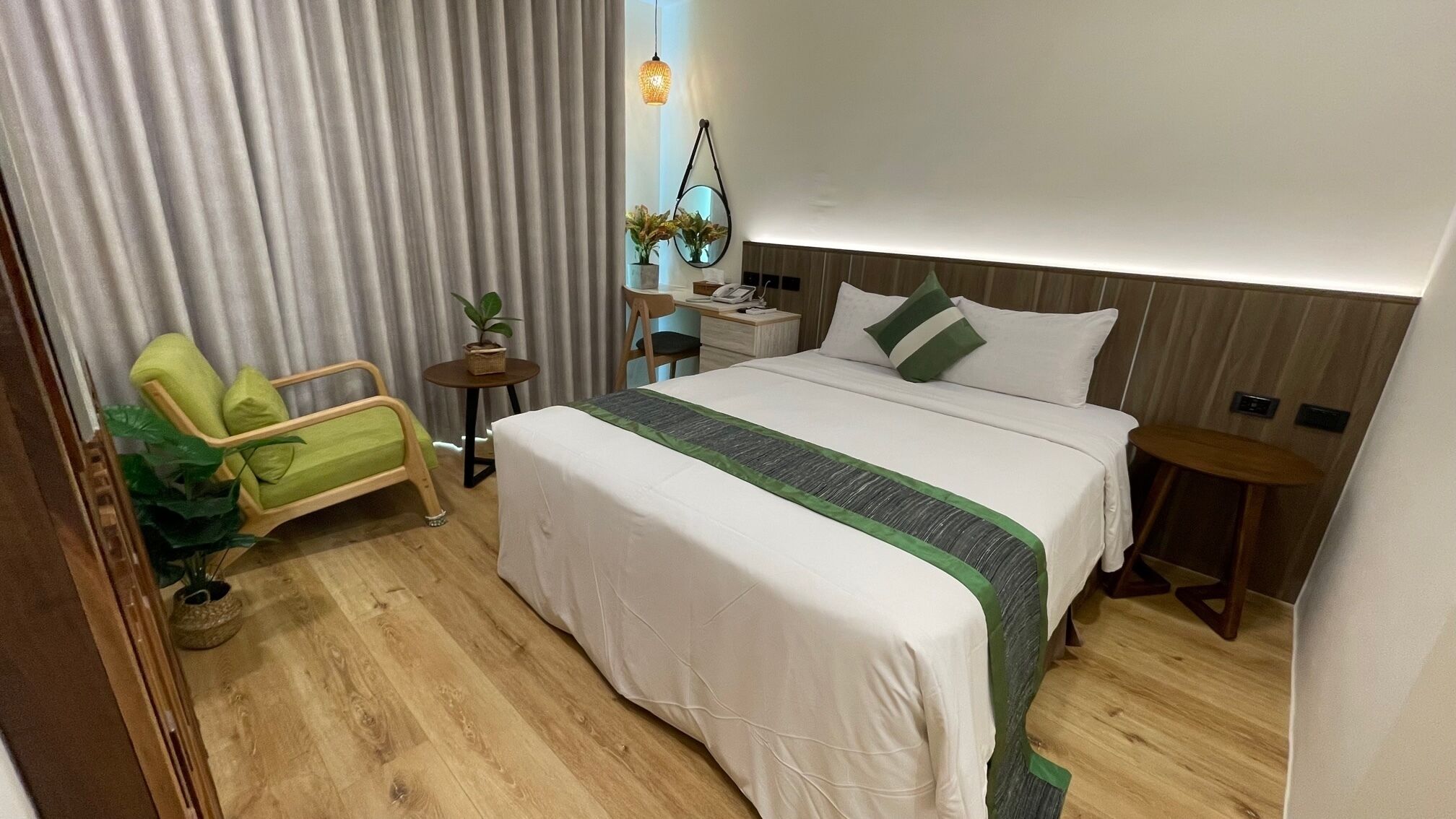 A hotel room with a bed, bedside tables, a chair, a small table with a plant, and a hanging light fixture.