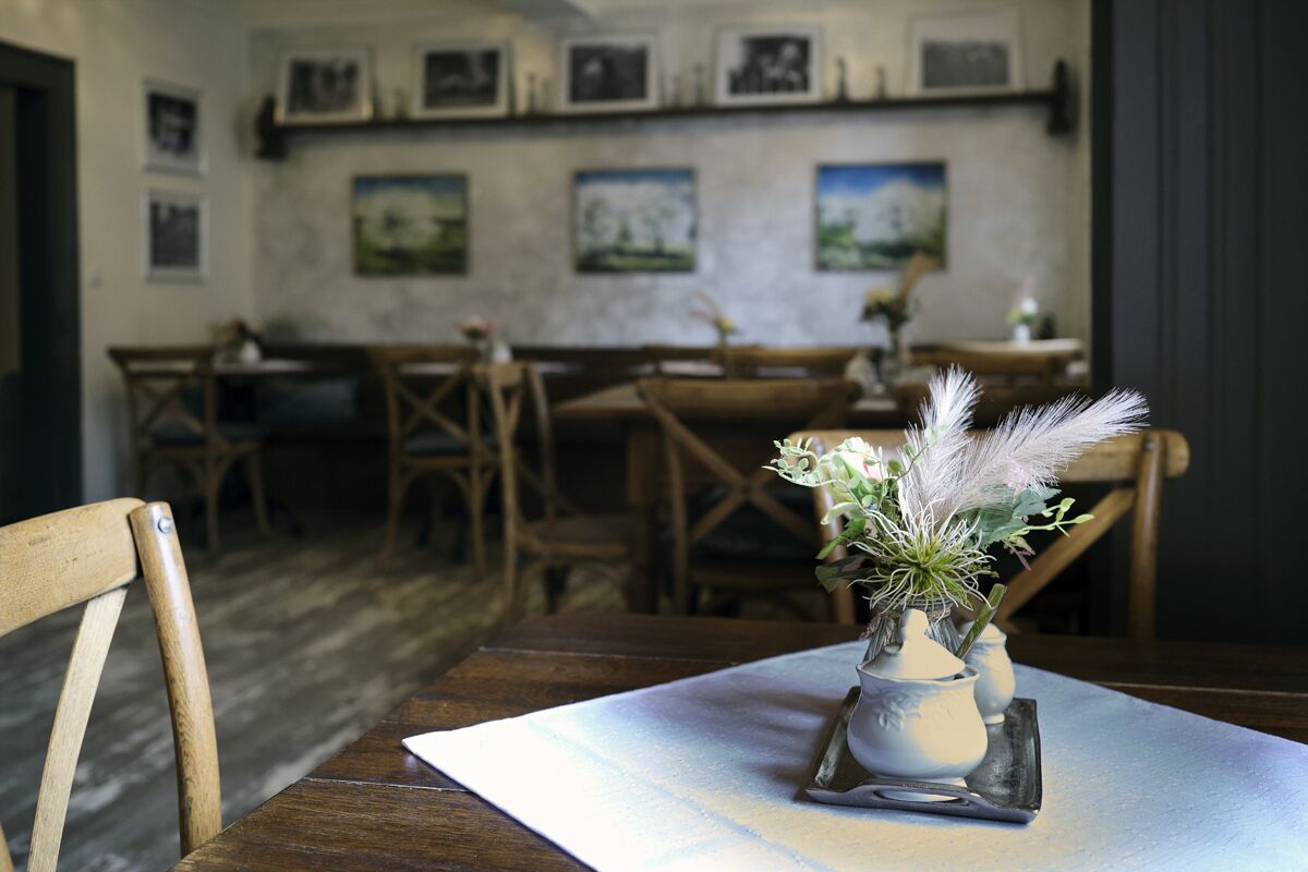 A dining area with wooden tables and chairs, a vase with flowers on a table, and framed pictures on the wall.