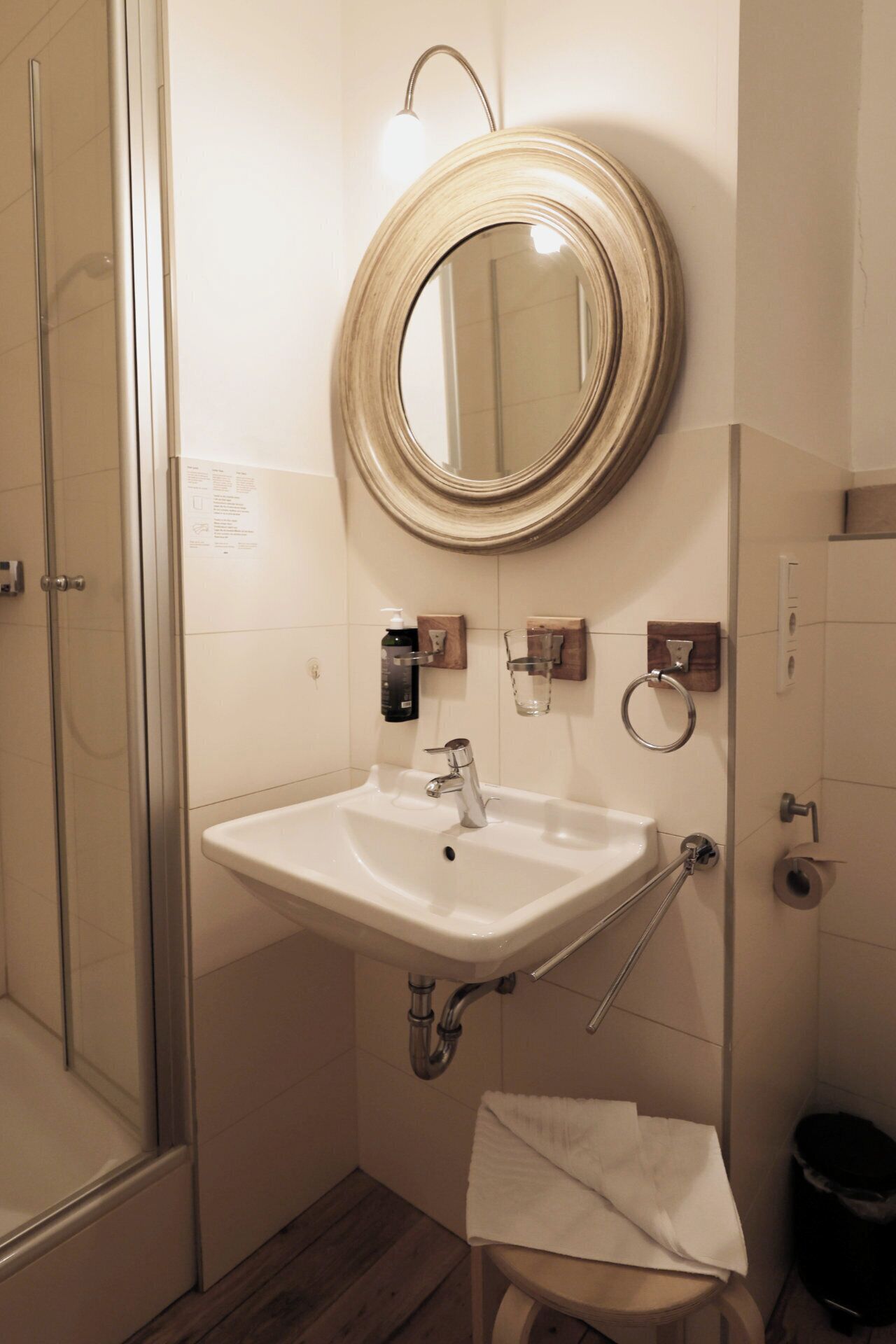 Une salle de bain avec un lavabo blanc, un miroir rond et une cabine de douche en verre.