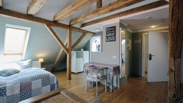 Een slaapkamer met een houten plafond, een bed met een sprei, een kleine tafel met stoel, en een deur naar een andere kamer.
