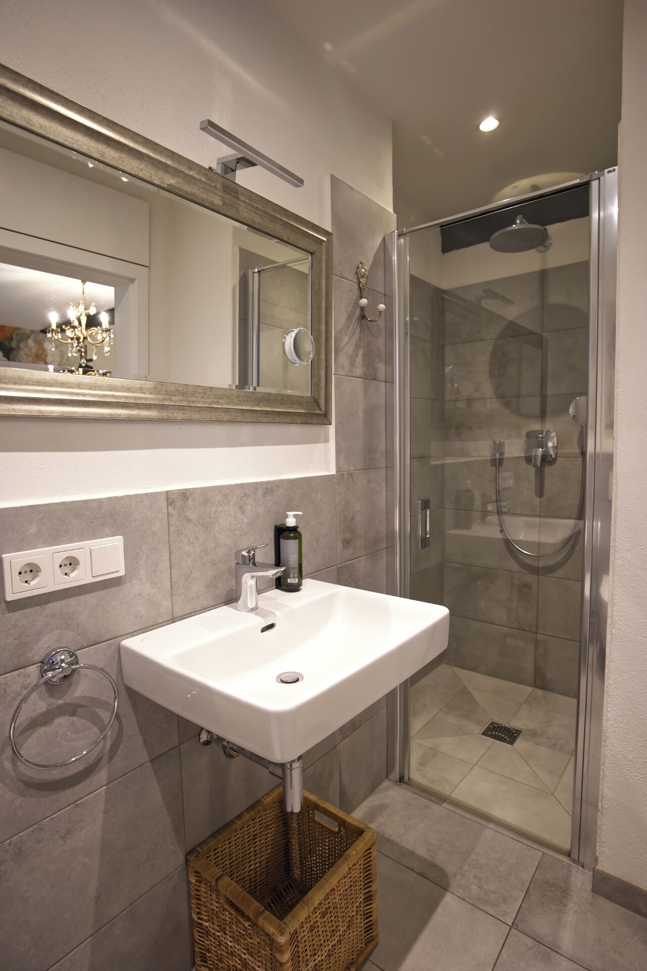 A modern bathroom with a white sink, a large mirror, a glass-enclosed shower, and a wicker basket.