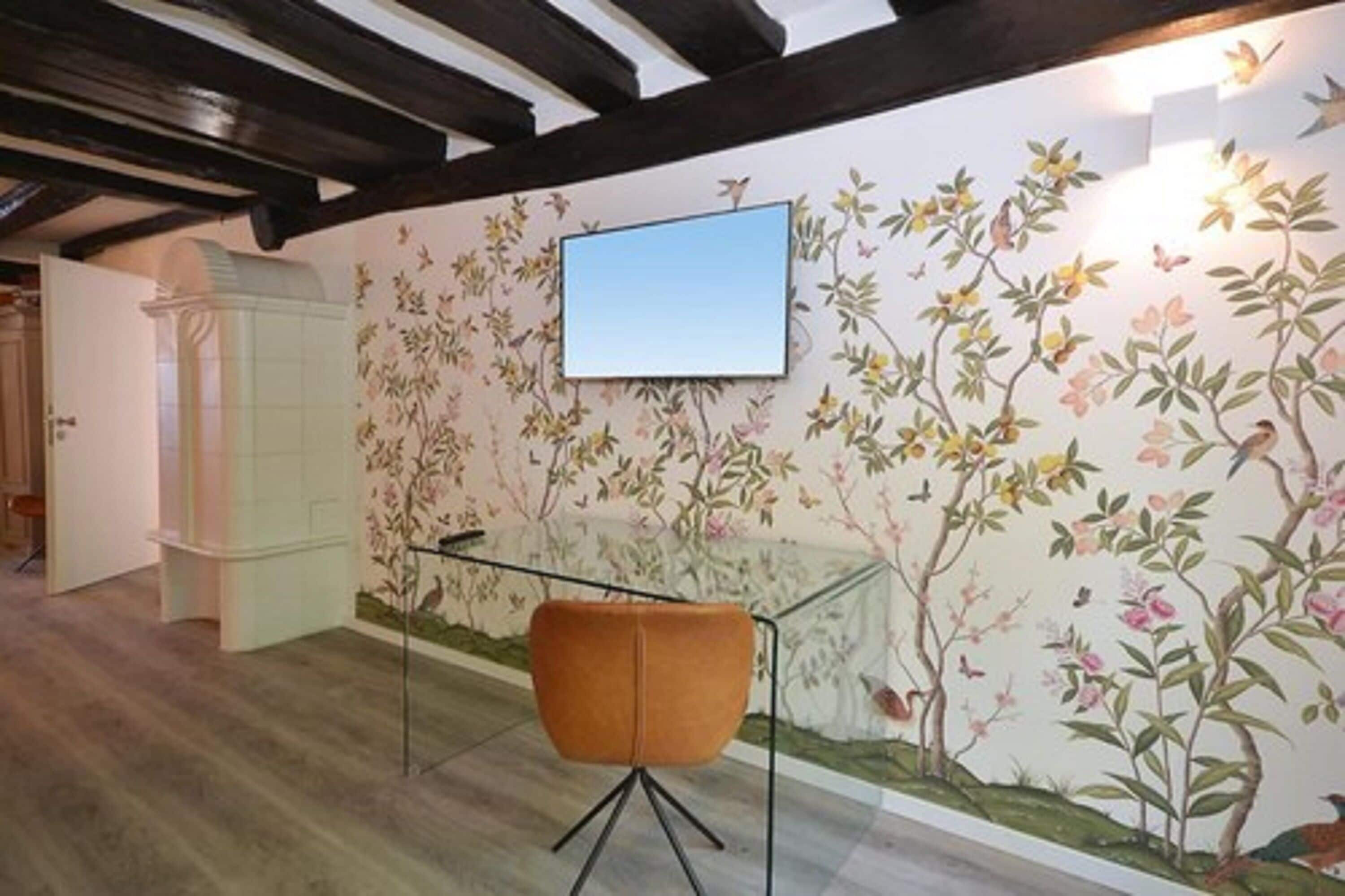 A room with a floral mural, a framed picture on the wall, and a modern chair.
