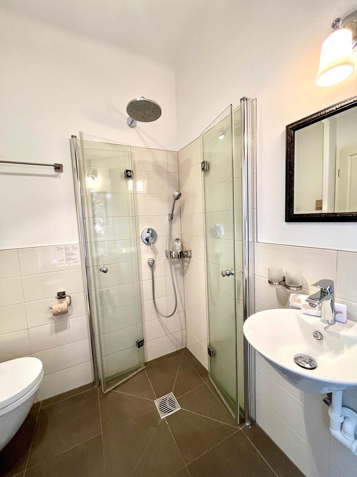 Un bagno moderno con doccia vetro, lavandino bianco e specchio sopra il lavandino.