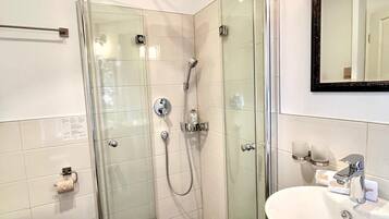 Un bagno moderno con doccia vetro, lavandino bianco e specchio sopra il lavandino.