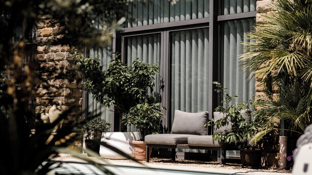 Un espace extérieur moderne aménagé avec un mur en pierre, de grandes fenêtres et divers pots de plantes.