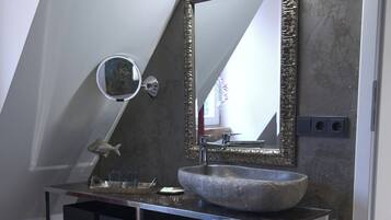Un baño moderno con un lavabo de piedra, un espejo grande y un espejo redondo pequeño.