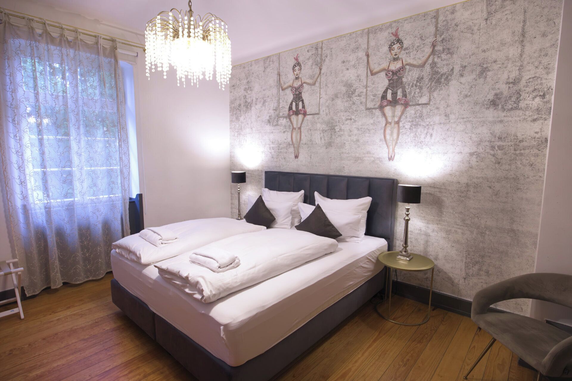 A hotel room with a large bed, two bedside lamps, a chandelier, and a wall with a textured mural.