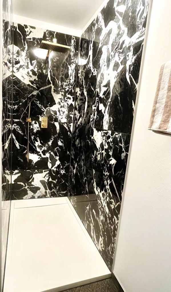 A bathroom with black and white marble walls, a shower area, and a towel rack.
