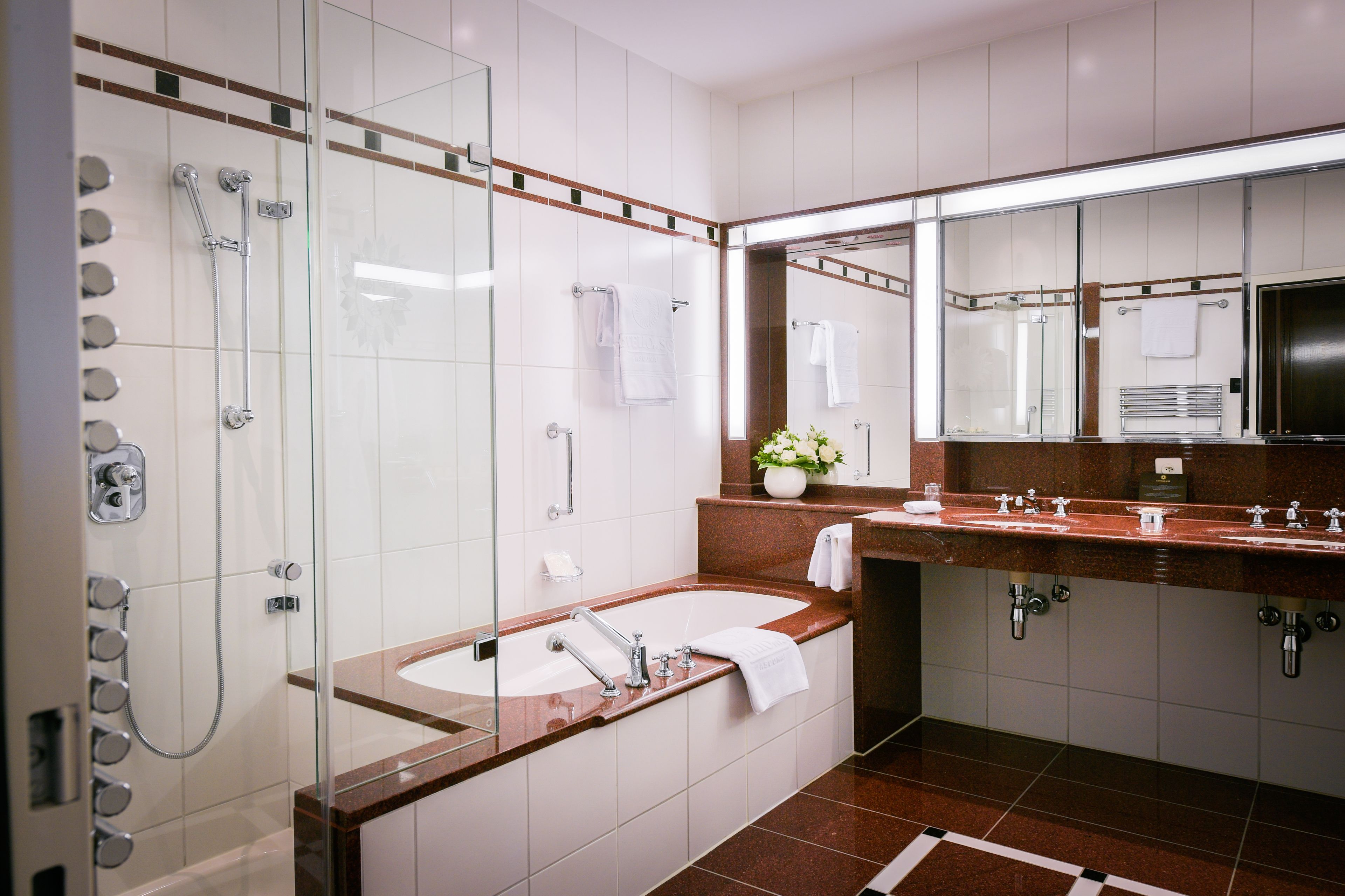 Un baño moderno con ducha envuelta en vidrio, lavabo de mármol y un espejo grande.