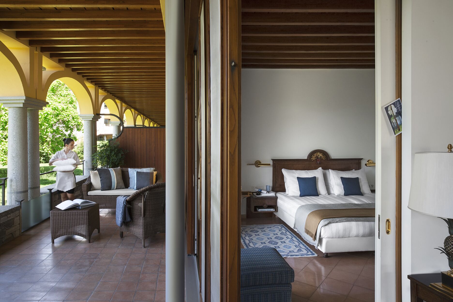 Habitación de hotel con cama, mesita de noche, lámpara y vistas al exterior.
