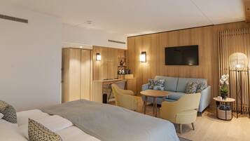 A modern hotel room with a large bed, a sofa, a small table, and a TV mounted on the wall.